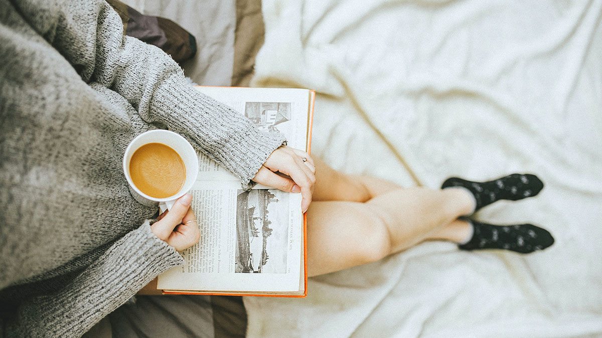 ragazza legge un libro sul divano col caffè in mano